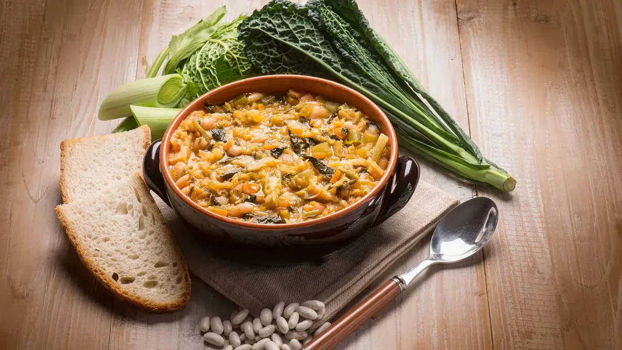 Piatto tipico toscano con pane raffermo: ribollita fumante in ciotola, contornata da fagioli, cavolo nero e porri.
