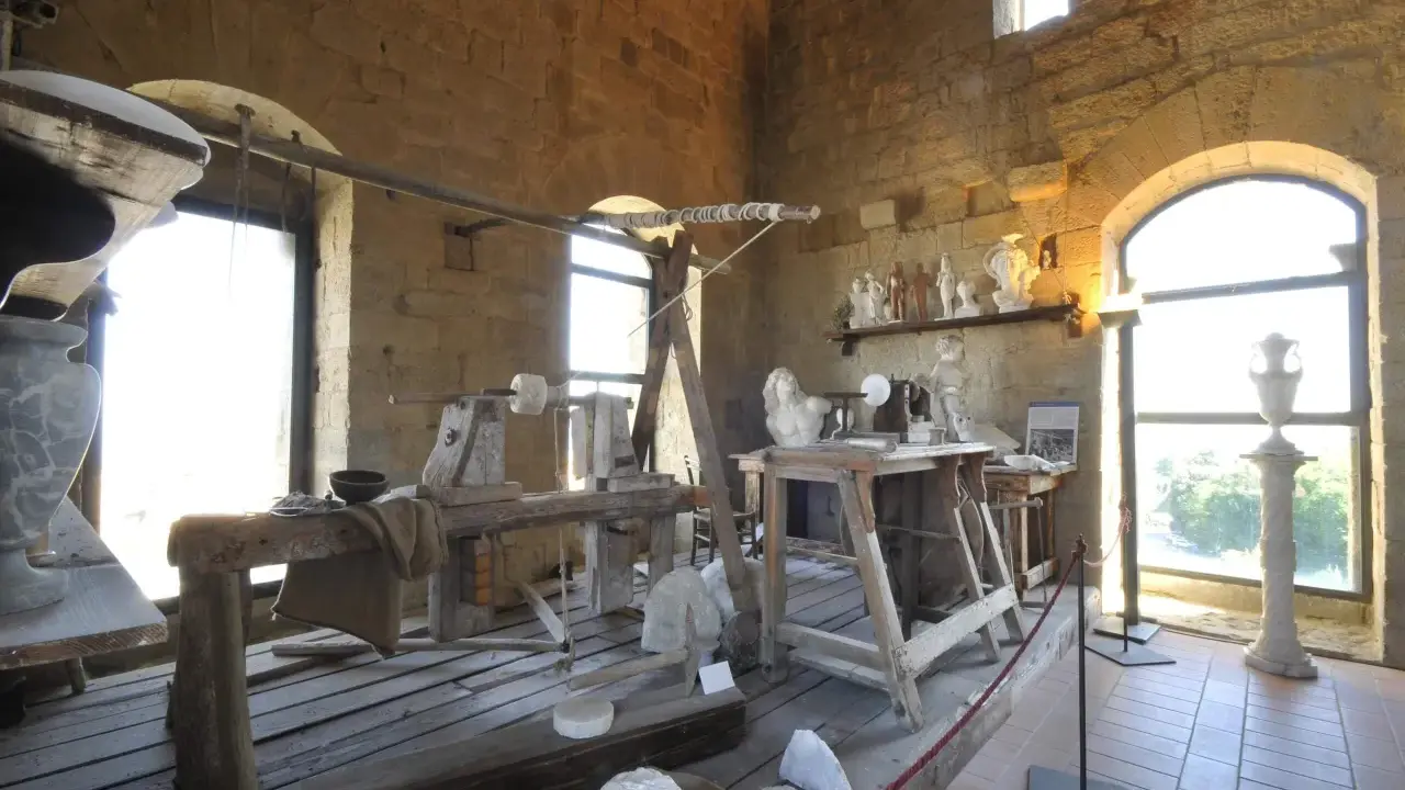 Laboratorio di scultura con attrezzi antichi e statue in marmo, che evoca la tradizione dell'alabastro toscana.