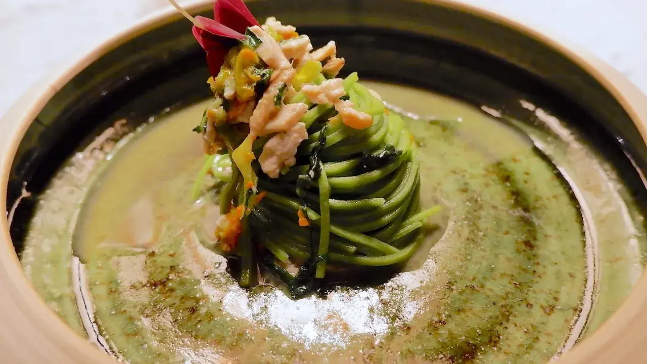 Un nido di spaghetti verdi con verdure e carne, guarnito con un fiore rosso. Un assaggio dei piatti tipici Avellino.