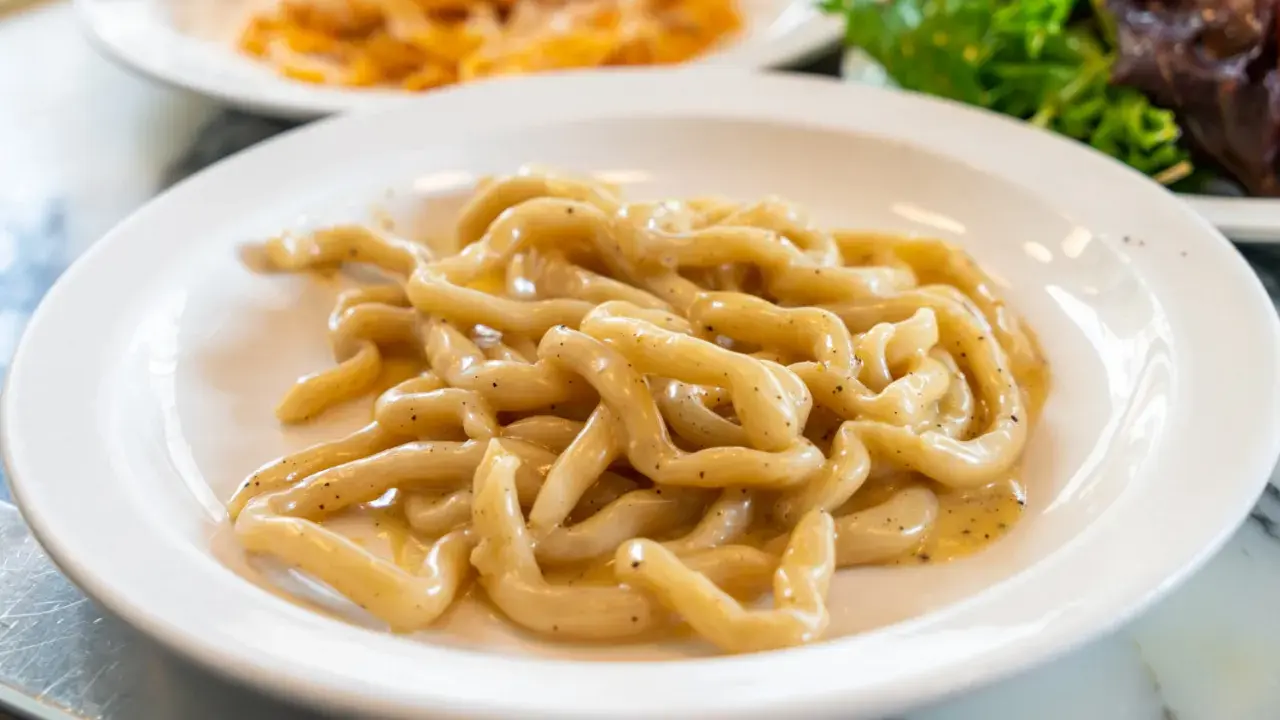 Pici cacio e pepe, un classico tra i piatti tipici di Siena, serviti su un piatto bianco.