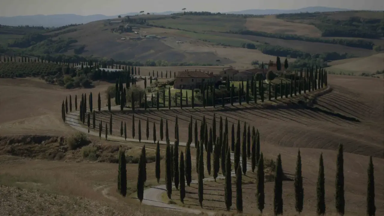 Un casale nel Val d'Orcia autunno, circondato da cipressi che disegnano curve sinuose su dolci colline.