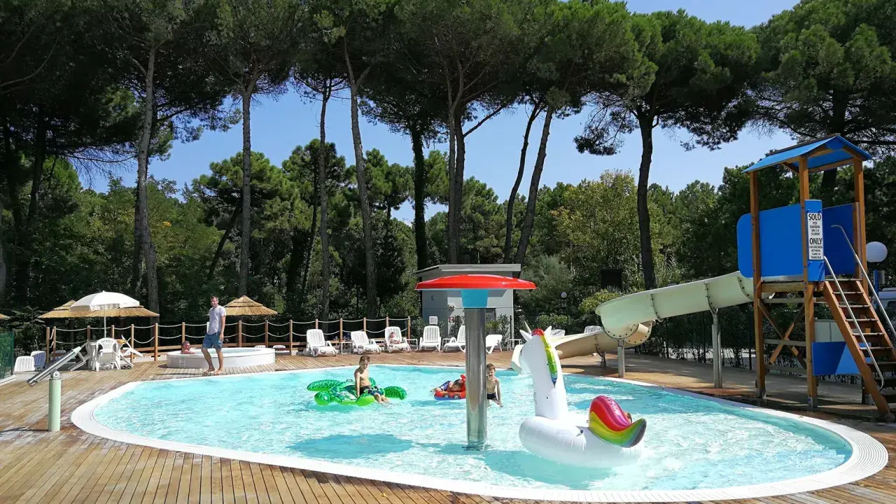 Bambini felici in piscina con gonfiabili, scivoli e giochi d'acqua. Perfetti campeggi Emilia Romagna per bambini, un'oasi di divertimento sotto i pini.