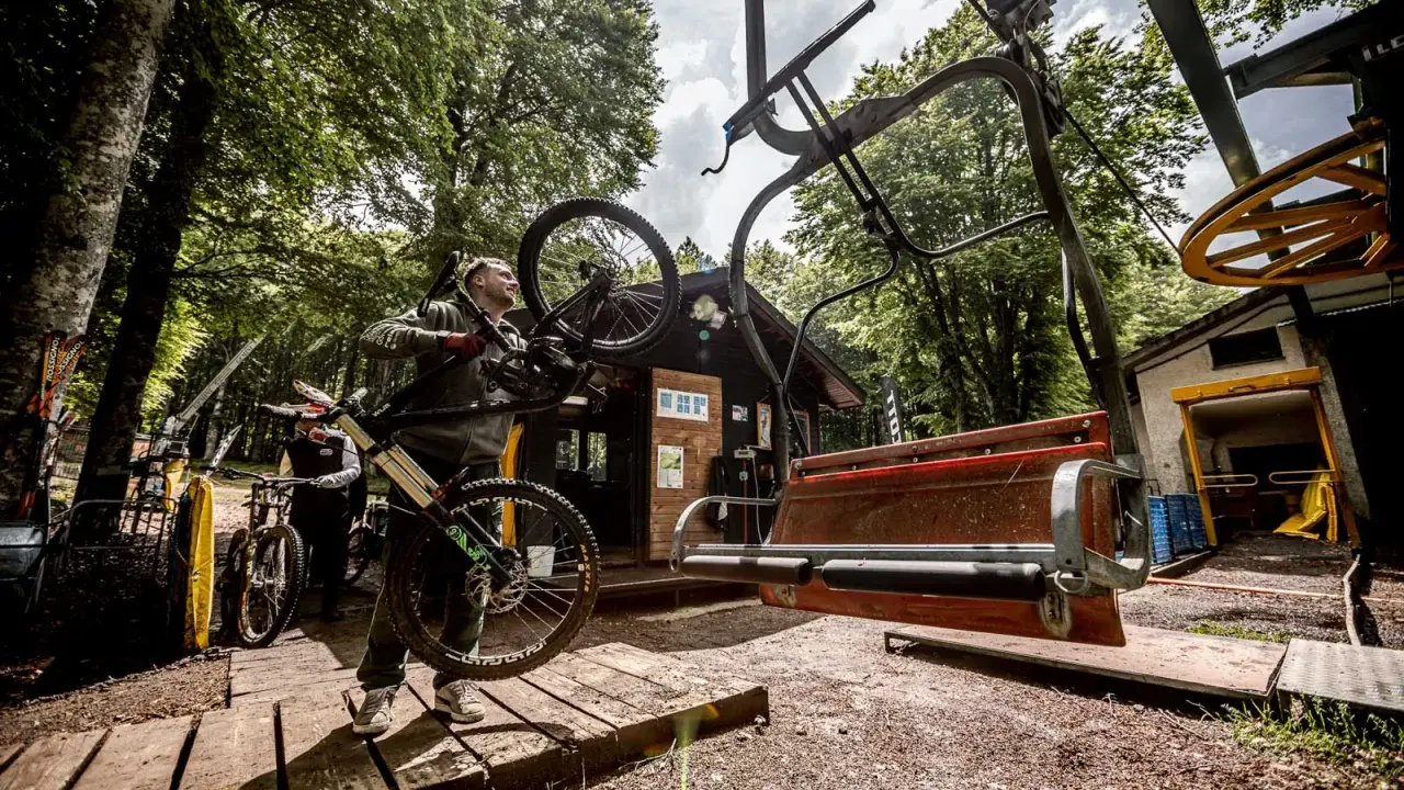 Ciclista porta la sua bici verso gli impianti di risalita ad Amiata, pronto per un'avventura in mountain bike.