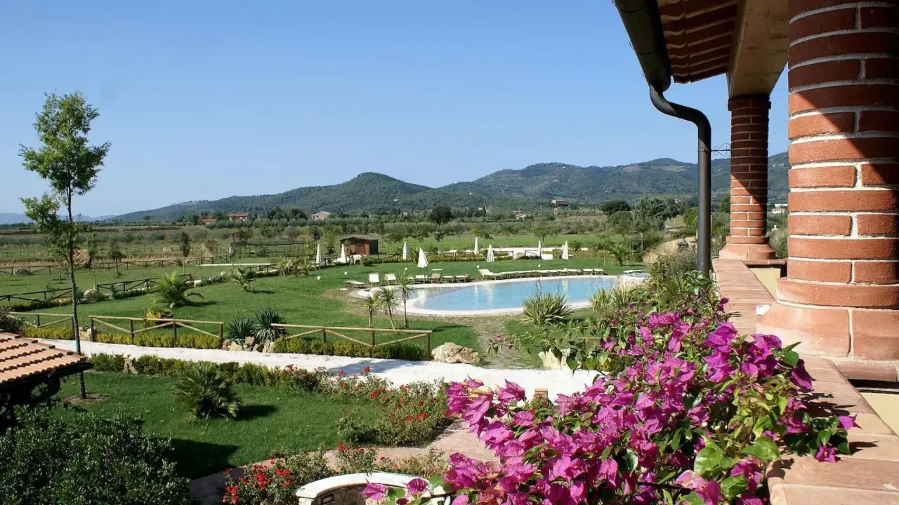 Un angolo di campagna toscana lungo il mare, con piscina, giardini curati e colline verdi all'orizzonte.