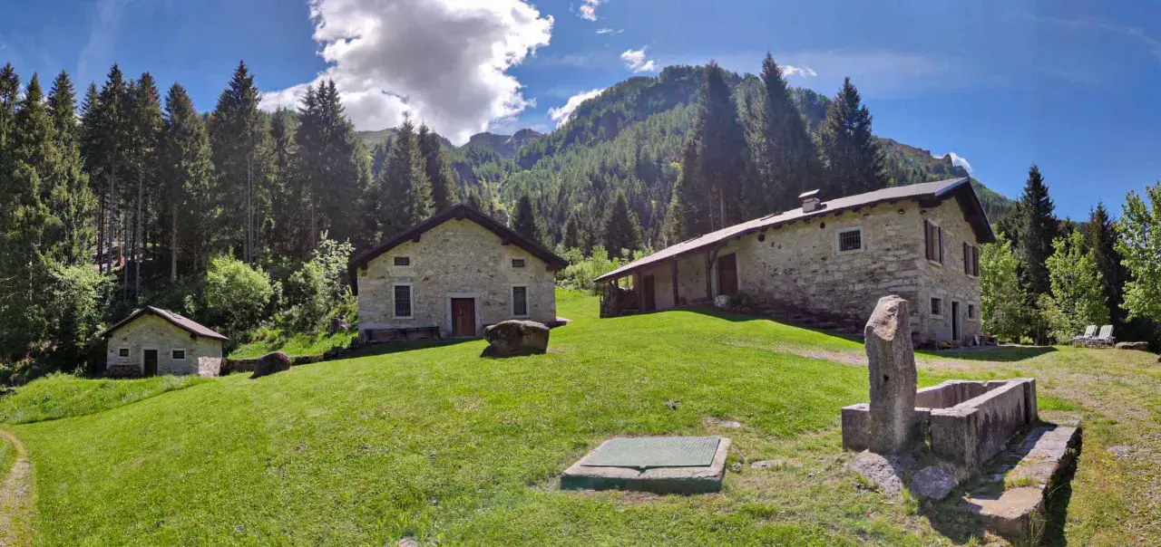 Agriturismi lombardia montagna: casette in pietra immerse nel verde, con boschi e montagne sullo sfondo.