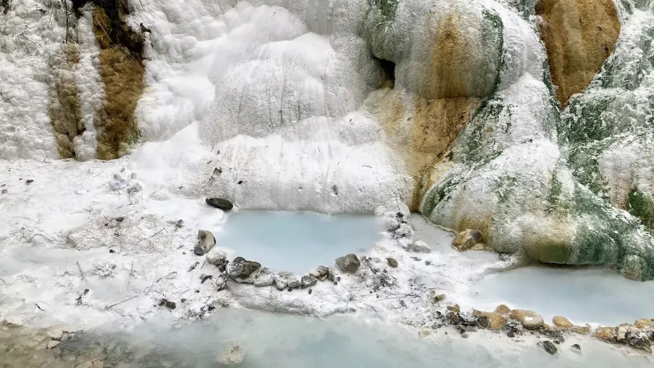 Cascate bianche e rocce calcaree ai Bagni San Filippo, con piccole pozze d'acqua azzurra che riflettono il paesaggio surreale.