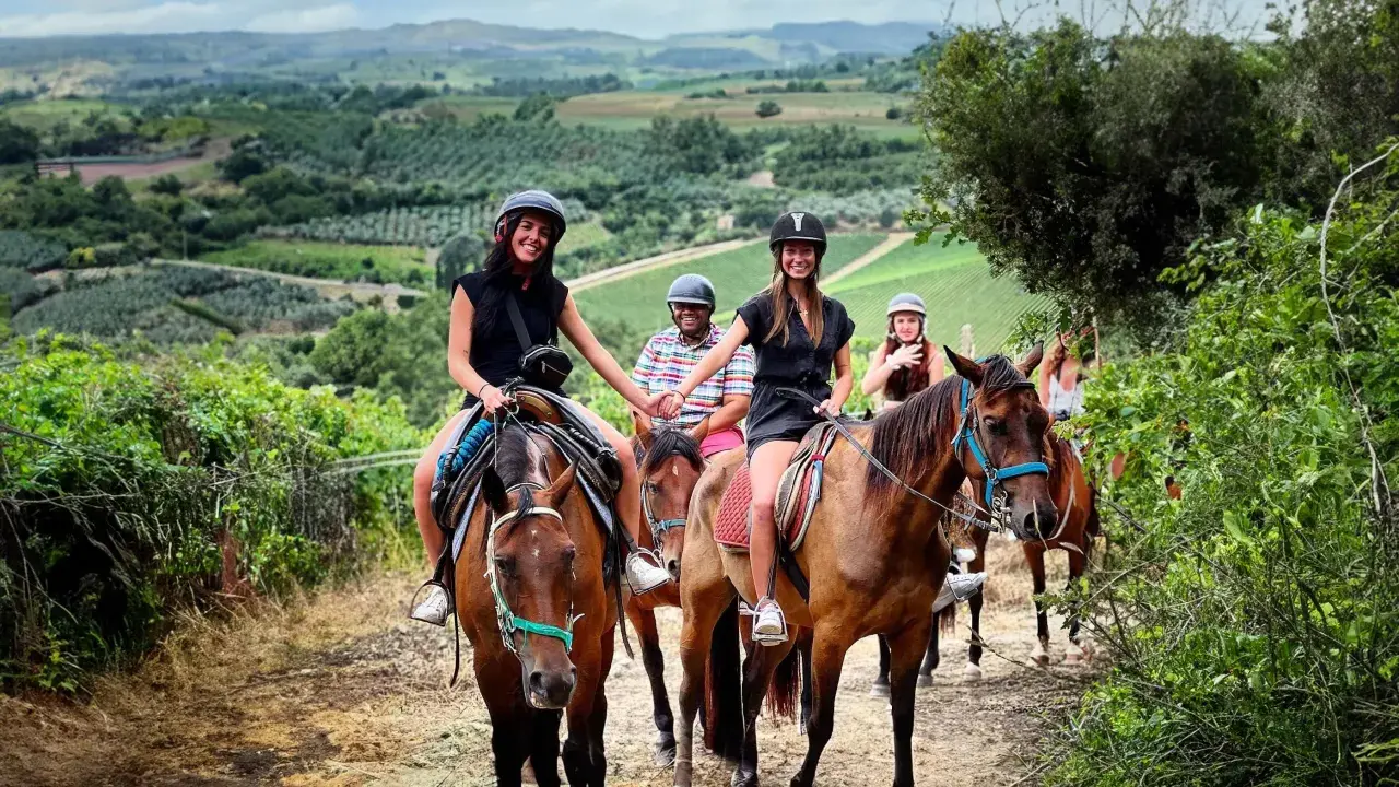 Un gruppo di amici si gode una **passeggiata a cavallo toscana** tra colline verdi e vigneti. Sorridono felici, immersi nella bellezza del paesaggio.
