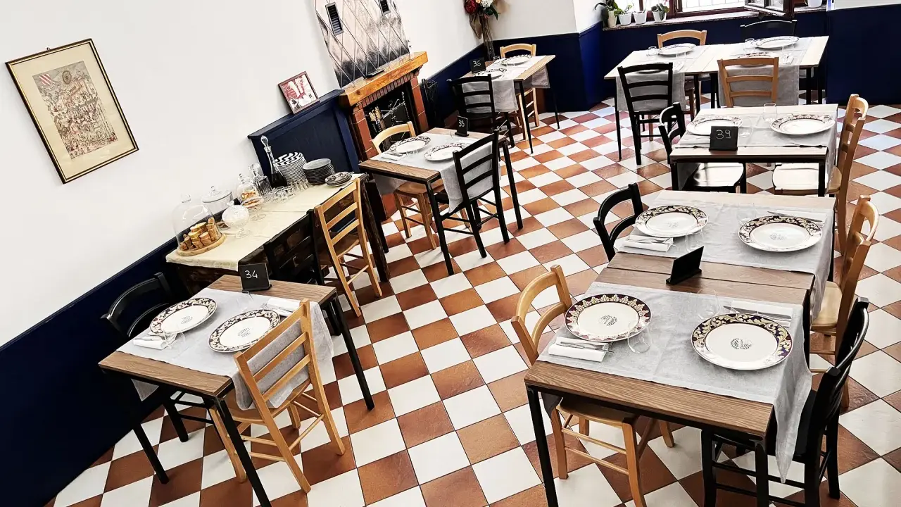 Tavoli apparecchiati in un ristorante, pronti per un'esperienza di **mangiare in Umbria**. Pavimento a scacchi, sedie in legno e dettagli eleganti.