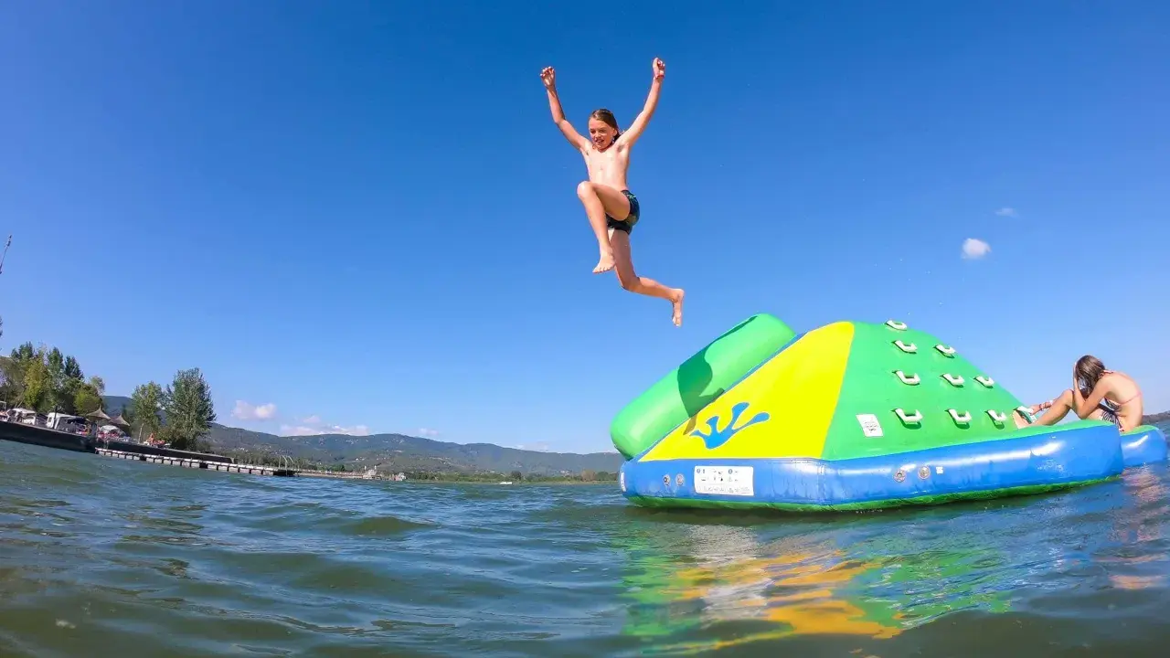 Bambini si divertono sul lago Trasimeno, uno salta da un gonfiabile mentre un altro si riposa.