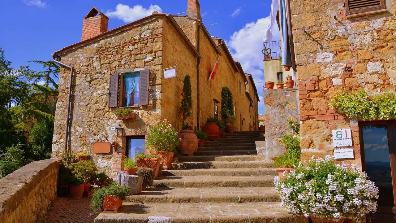 Pienza cosa vedere: scalinata in pietra con vasi di fiori e case in tufo sotto un cielo azzurro.