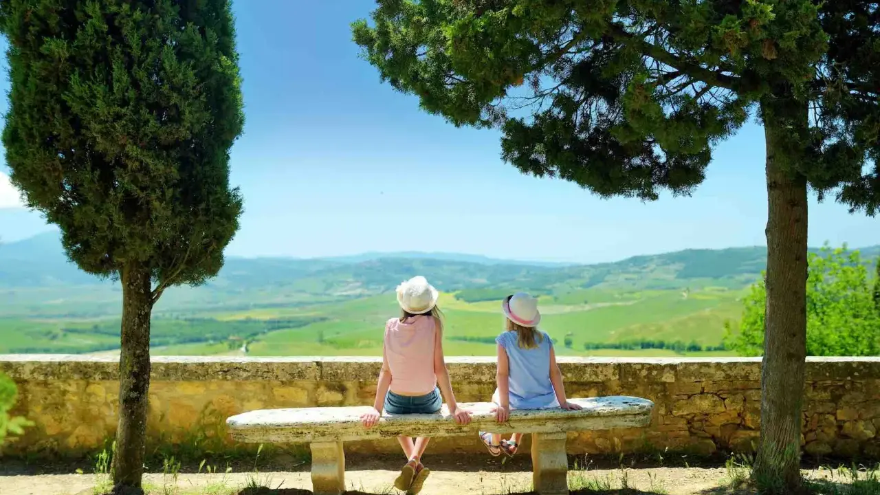 Due bambine con cappello ammirano il panorama collinare toscano, un perfetto weekend con bambini in Toscana.