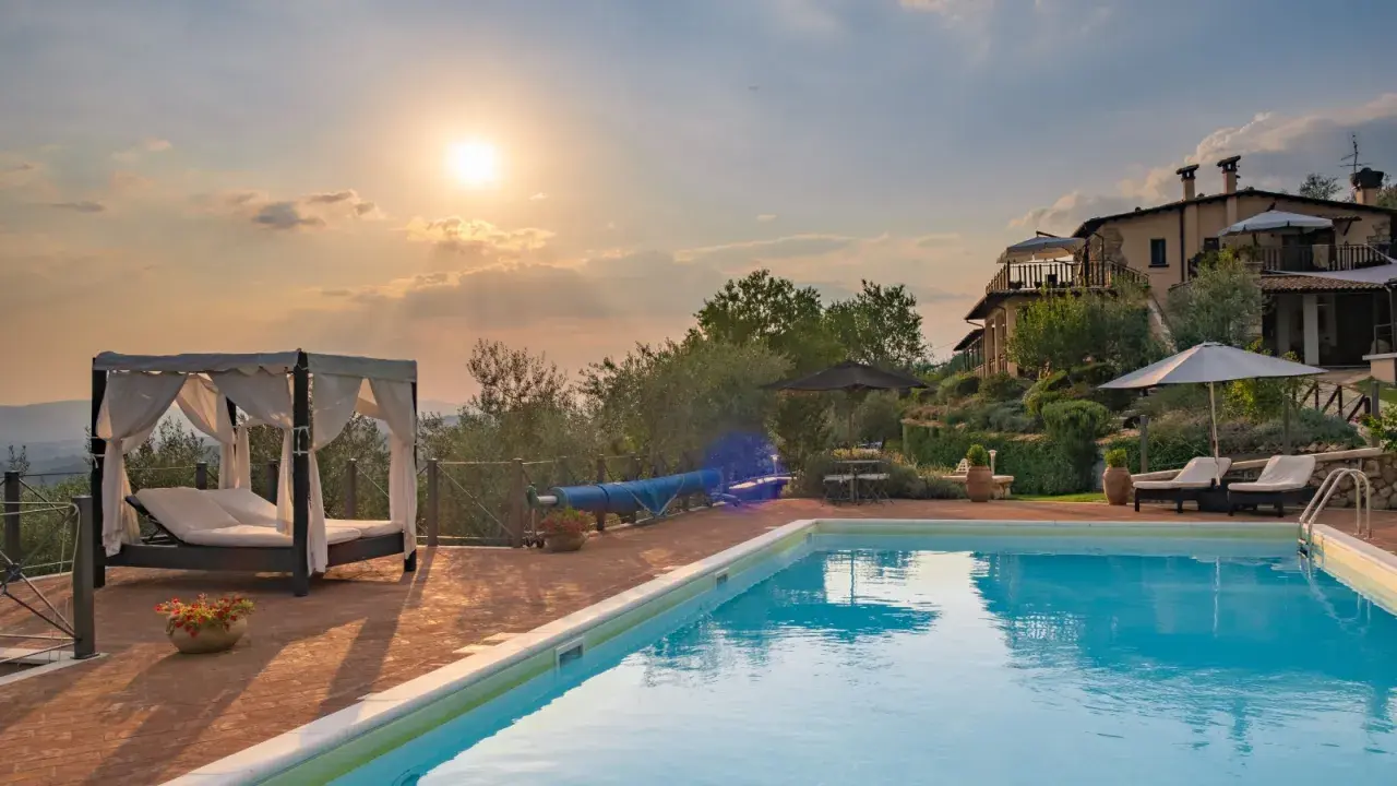 Piscina con lettini e gazebo, ideale per sapere dove dormire in Toscana. Tramonto suggestivo su un casale.