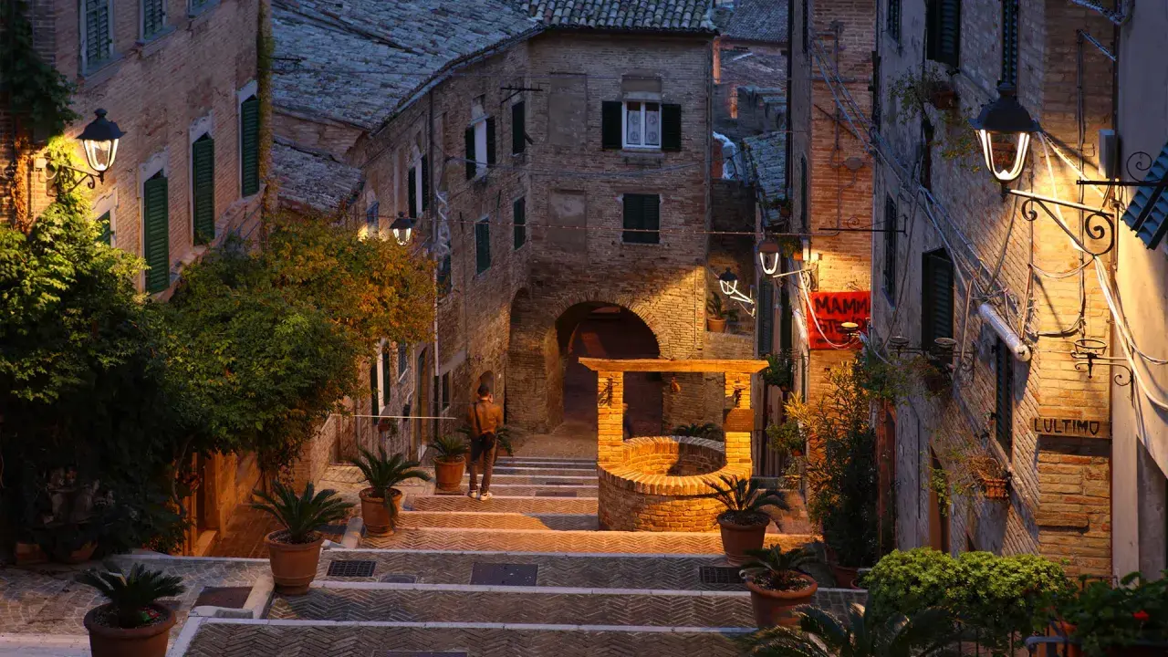 Un vicolo suggestivo a Montefeltro, cosa vedere: un pozzo antico, scalinate in pietra e luci soffuse creano un'atmosfera magica.