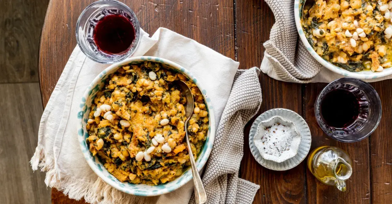 Un piatto fumante di fagioli e verdure, un classico delle ricette toscane, accompagnato da vino rosso e olio d'oliva.