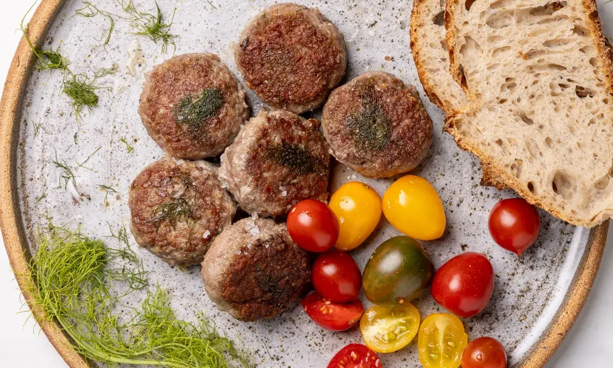 Polpette di cinta senese su piatto rustico, con pomodorini colorati, pane casereccio e finocchietto selvatico.