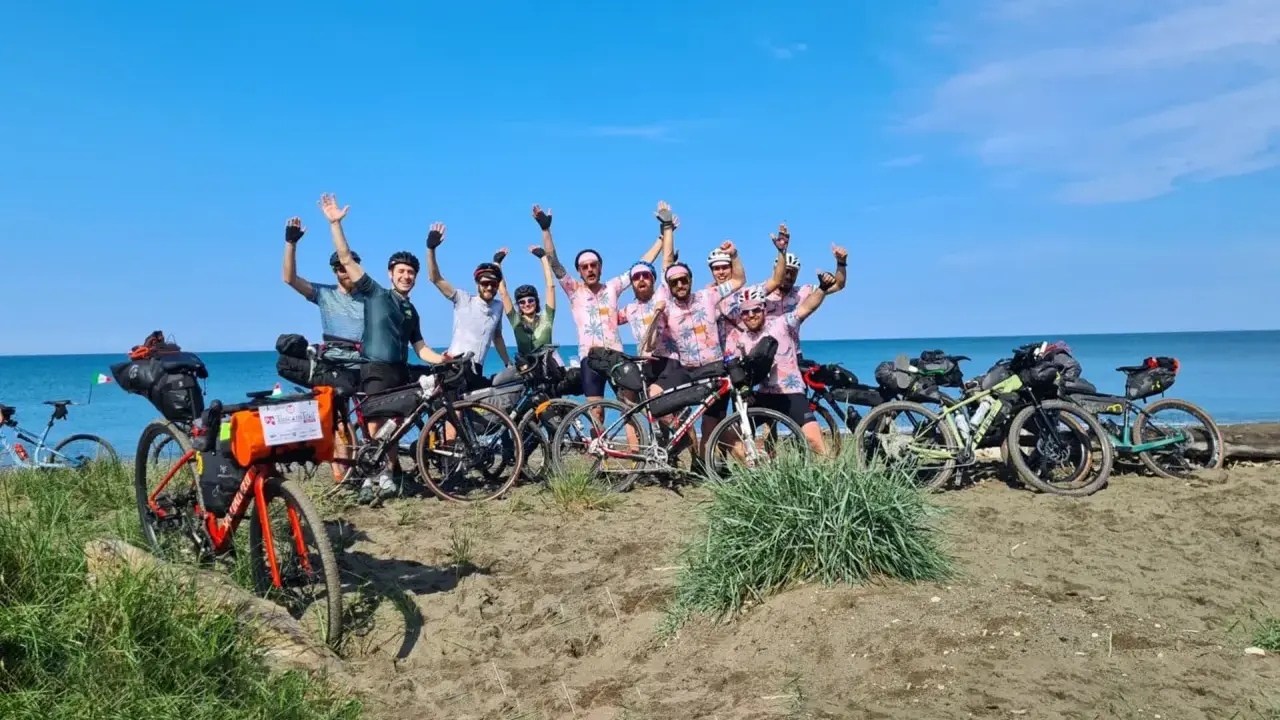 Un gruppo di ciclisti festeggia sulla spiaggia, pronti per un'avventura di cicloturismo in Toscana.