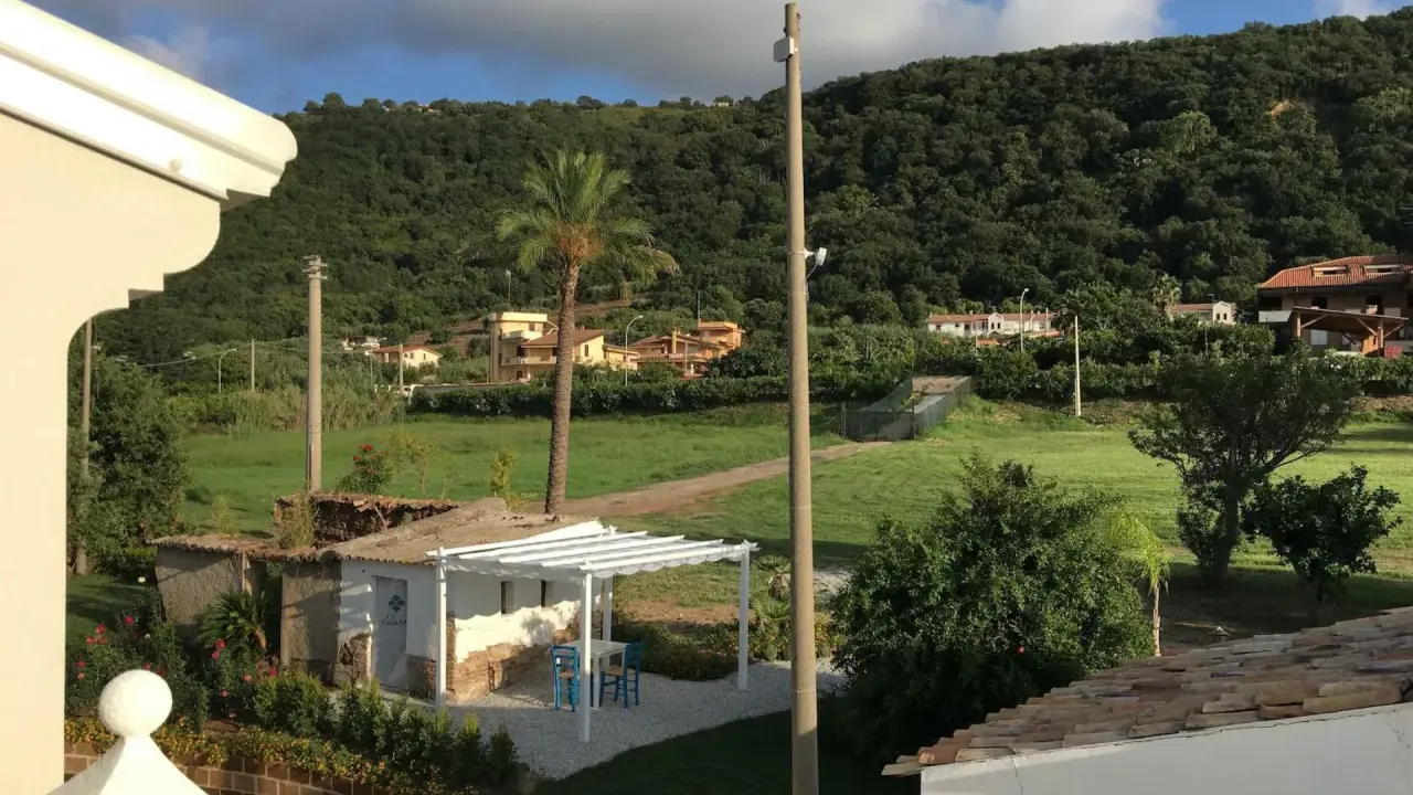 Un angolo di pace tra gli agriturismi in Calabria. Un pergolato bianco con tavolino e sedie blu, circondato da verde e colline rigogliose.