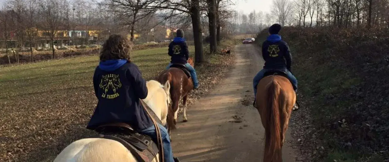 Cavalcata autunnale nei maneggi Piemonte, tre persone a cavallo su un sentiero sterrato tra alberi spogli e campi.