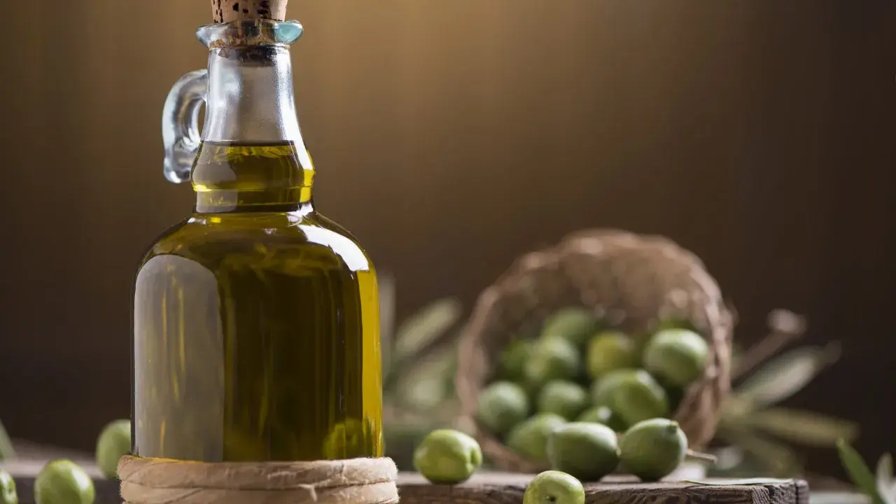 Bottiglia di olio extravergine di oliva, con olive verdi in cestino e su tagliere. La differenza tra olio di oliva e extravergine è la qualità.