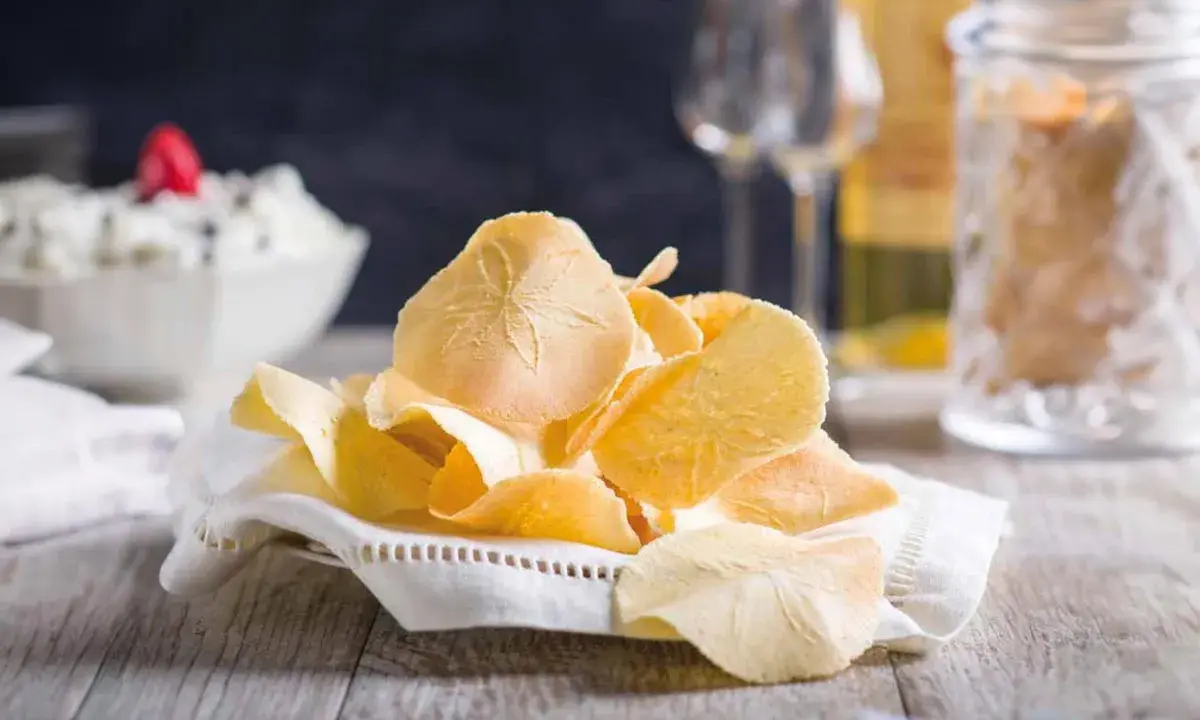 Delicati cialde, un dolce tipico toscano, su un tovagliolo ricamato. Sullo sfondo, una ciotola con crema e bicchieri.