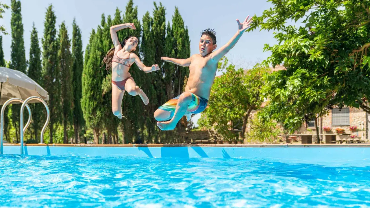 Bambini che saltano in piscina, una gioiosa Pasqua in Toscana tra cipressi e sole.