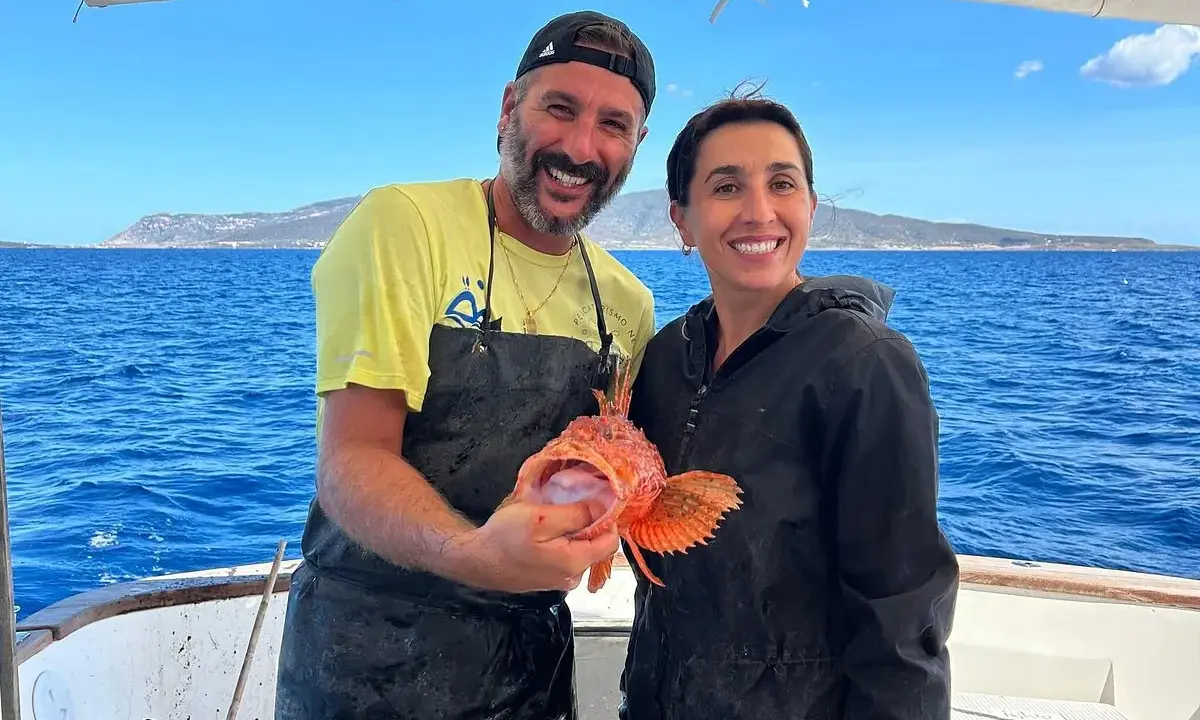 Coppia felice in barca, lui mostra un pesce rosso appena pescato, un'esperienza di pesca turismo indimenticabile.