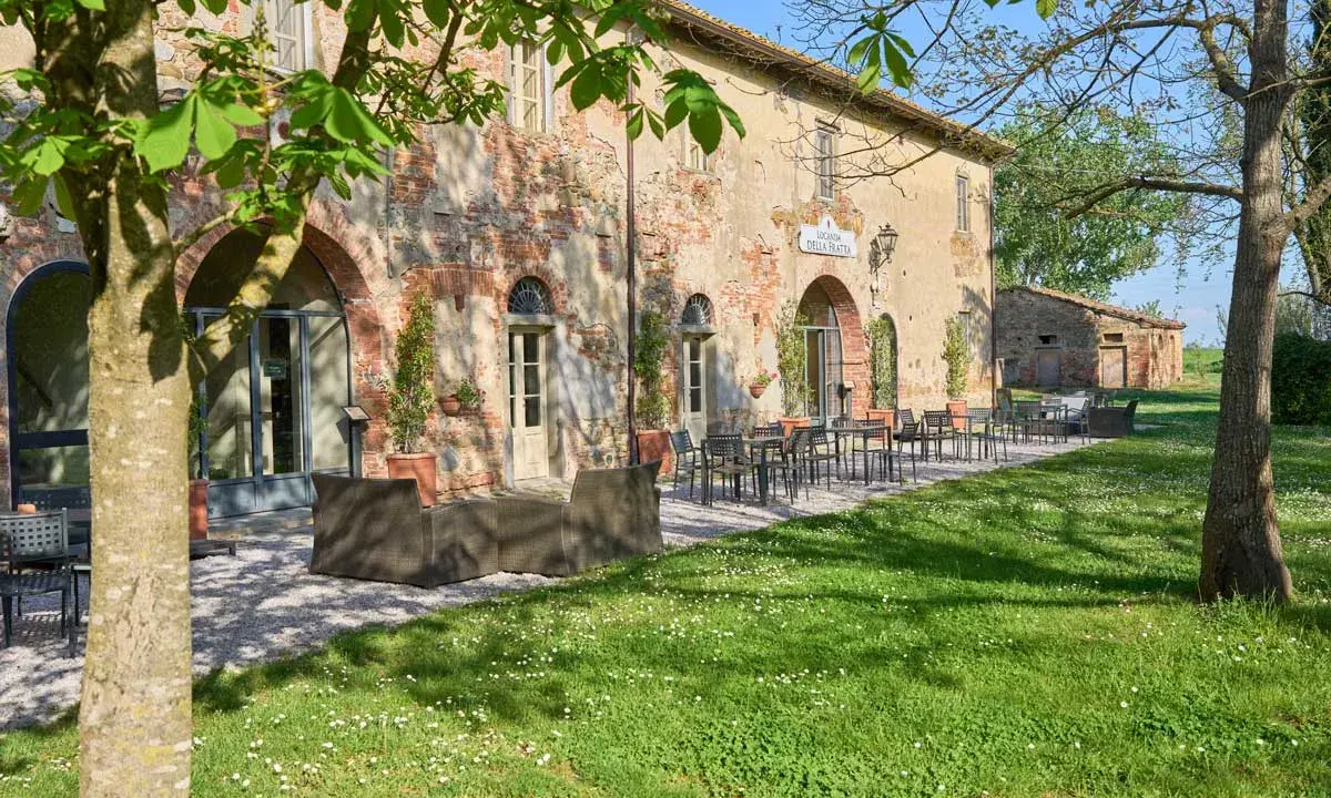 Antica locanda nel Val di Chiana, con tavoli all'aperto e un prato fiorito.