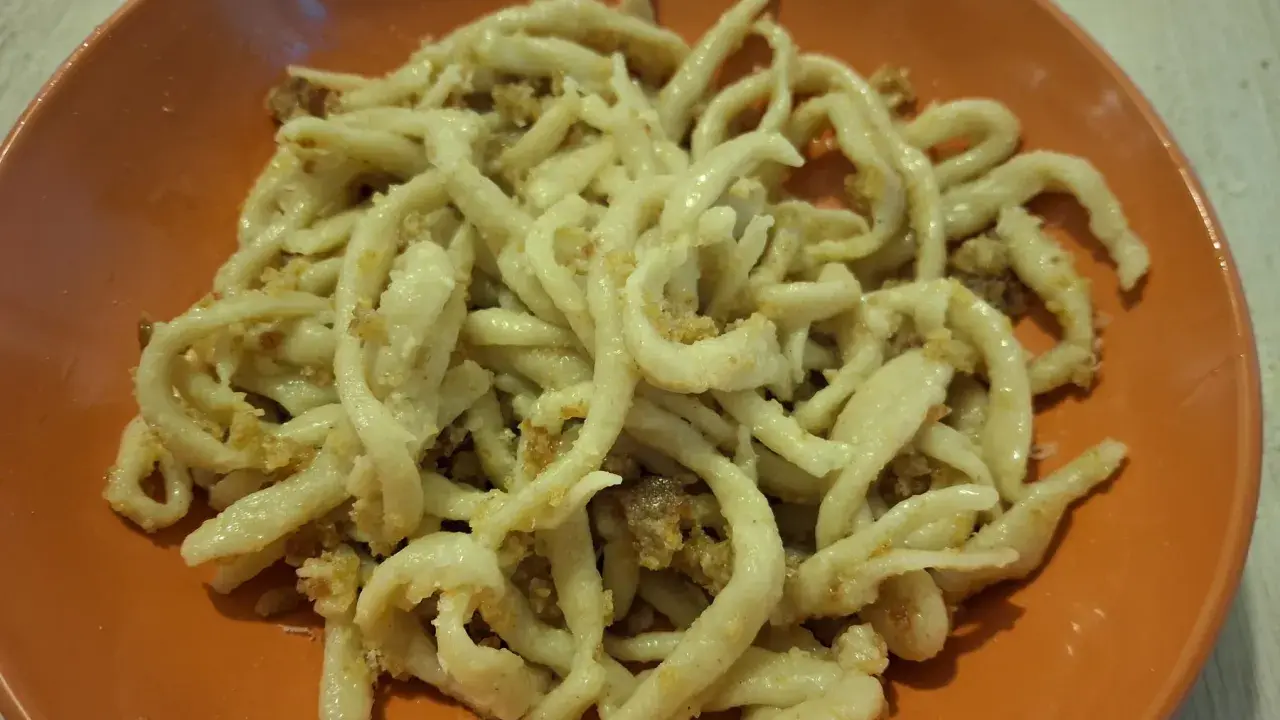 Pici fatti in casa con un saporito sugo per i pici, serviti in un piatto arancione.