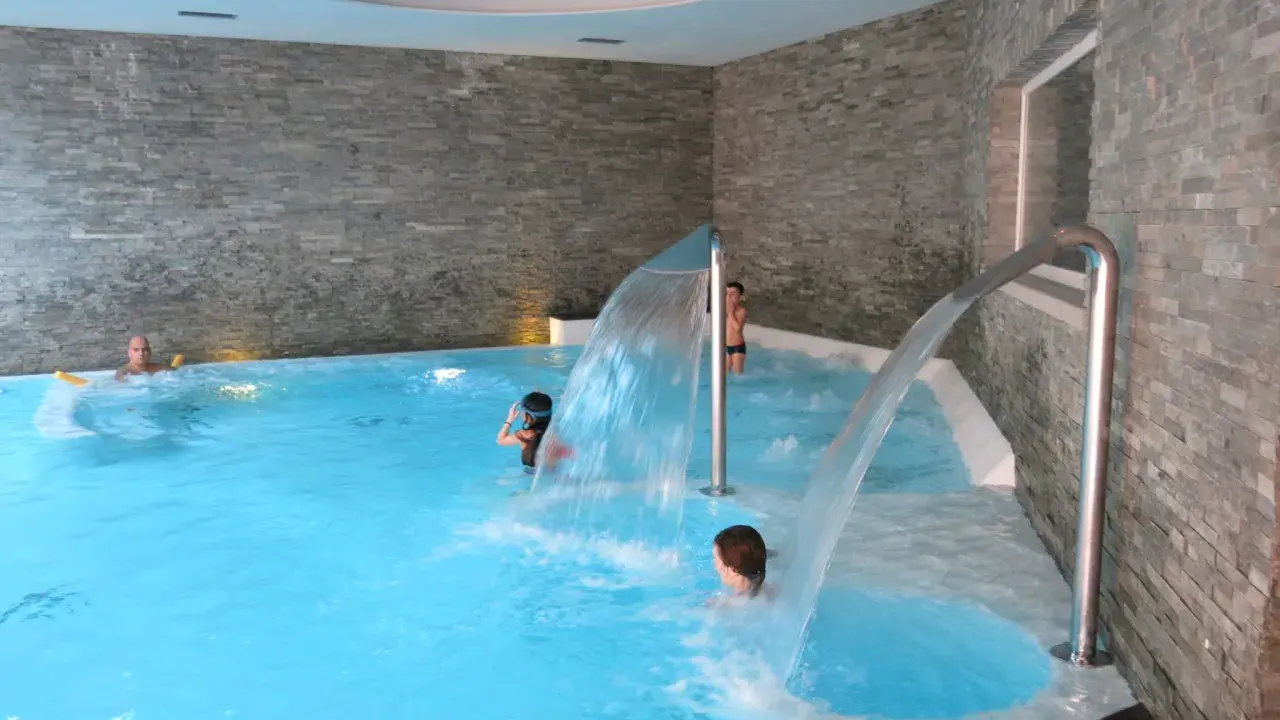 Bambini si divertono sotto cascate d'acqua in una piscina interna, un'ottima spa per famiglie in Lombardia.