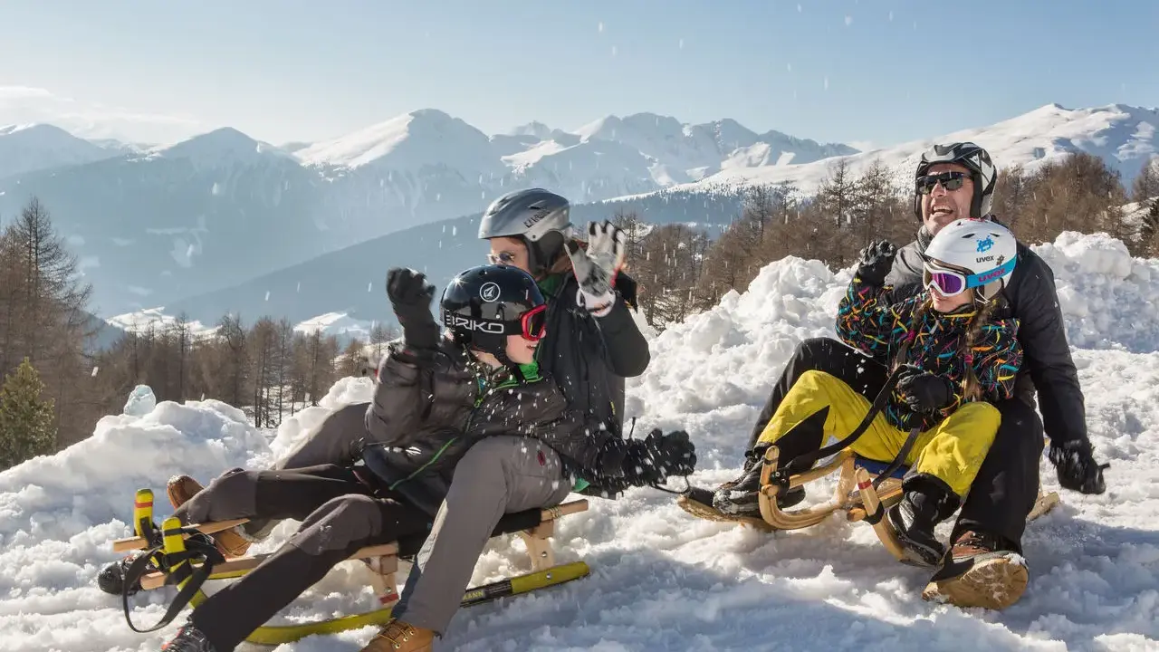 Famiglia felice in slittino sulla montagna per bambini in estate, con neve e montagne innevate sullo sfondo.