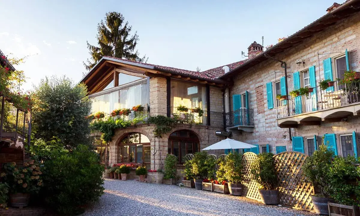 Un incantevole agriturismo in Piemonte, con un cortile acciottolato, balconi fioriti e persiane azzurre.