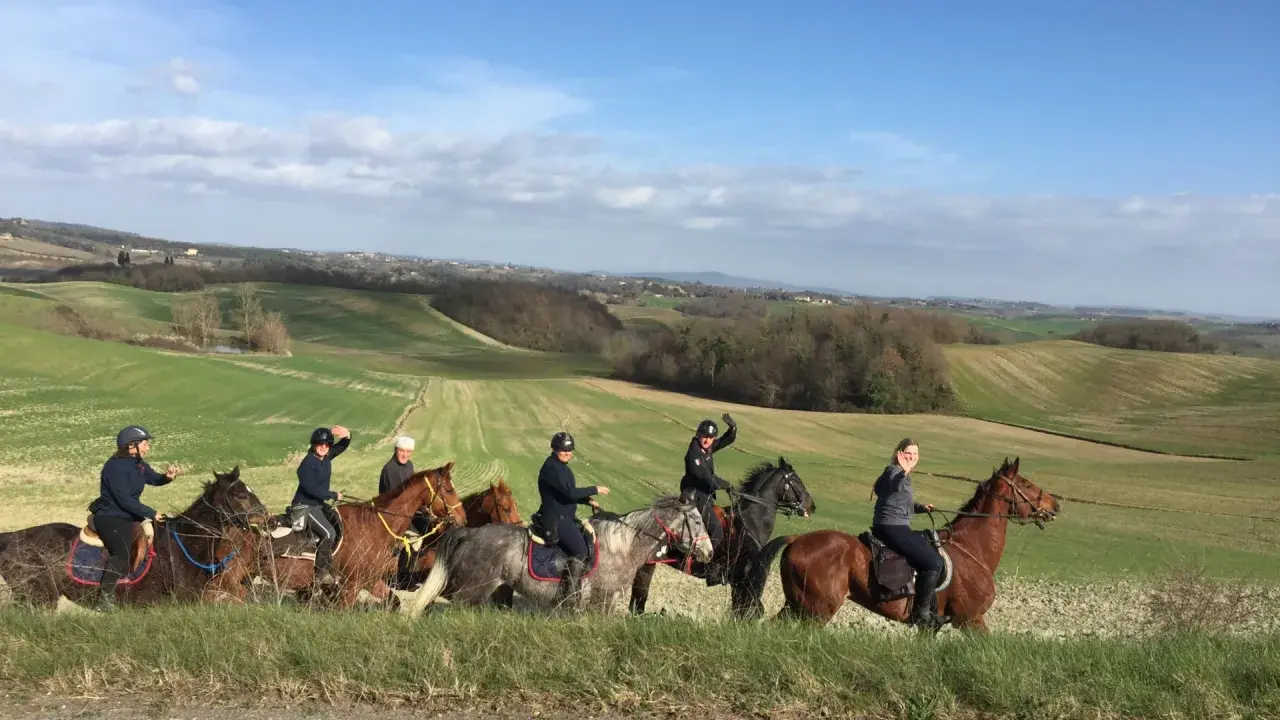 Un gruppo di persone in sella a cavalli attraversa un paesaggio collinare verdeggiante, godendosi le loro vacanze a cavallo sotto un cielo azzurro.
