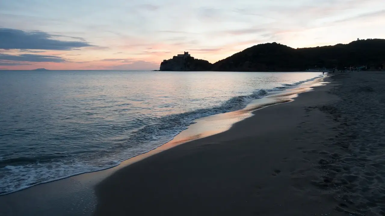 Tramonto sulla costa della Toscana, con un castello su una collina e il mare calmo. Un ricordo di vacanza con un neonato.