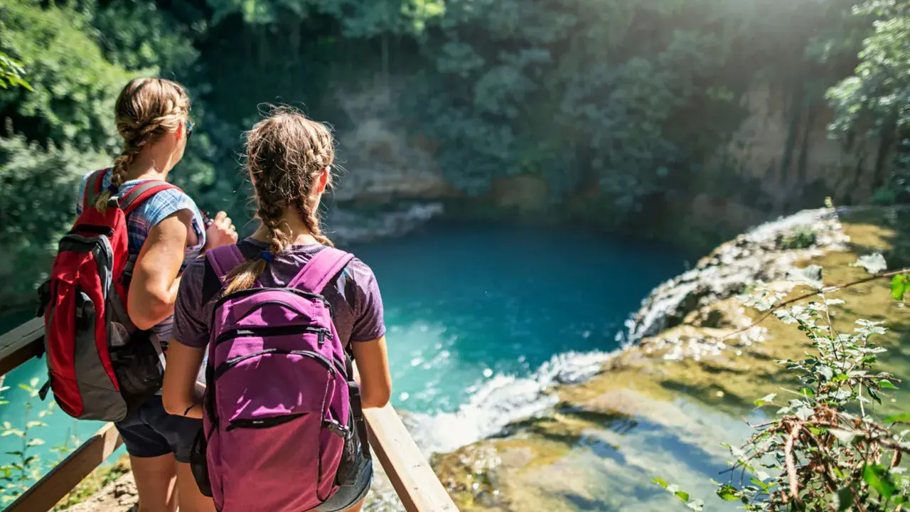 Due ragazze con zaini ammirano una cascata durante un trekking in Toscana montagna.