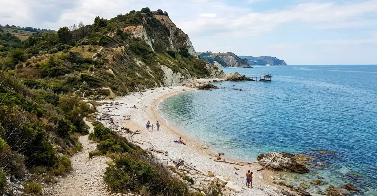 Spiaggia di sassi con scogliere verdi, ideale per escursioni nelle Marche. Famiglie passeggiano e si rilassano al sole.
