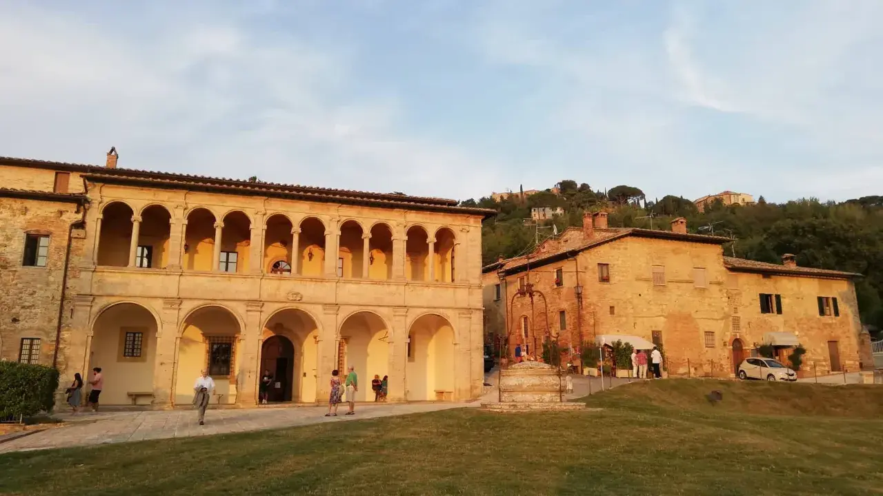 Edificio storico con portico ad archi, un pozzo e persone che passeggiano. Un luogo che sembra uscito da uno dei tanti film girati a Montepulciano.