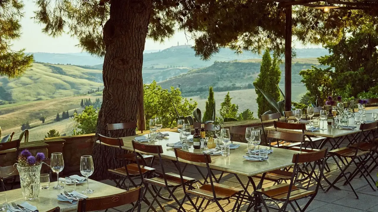 Tavoli apparecchiati sotto un pergolato con vista sulle colline toscane. Un'atmosfera perfetta per gustare i sapori degli agriturismi in Toscana.
