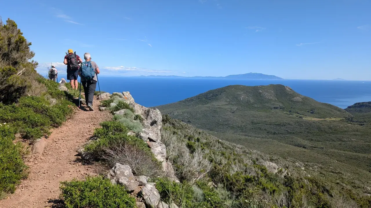 Persone in cammino su sentiero panoramico, godendosi le camminate organizzate in Toscana con vista sul mare e isole.