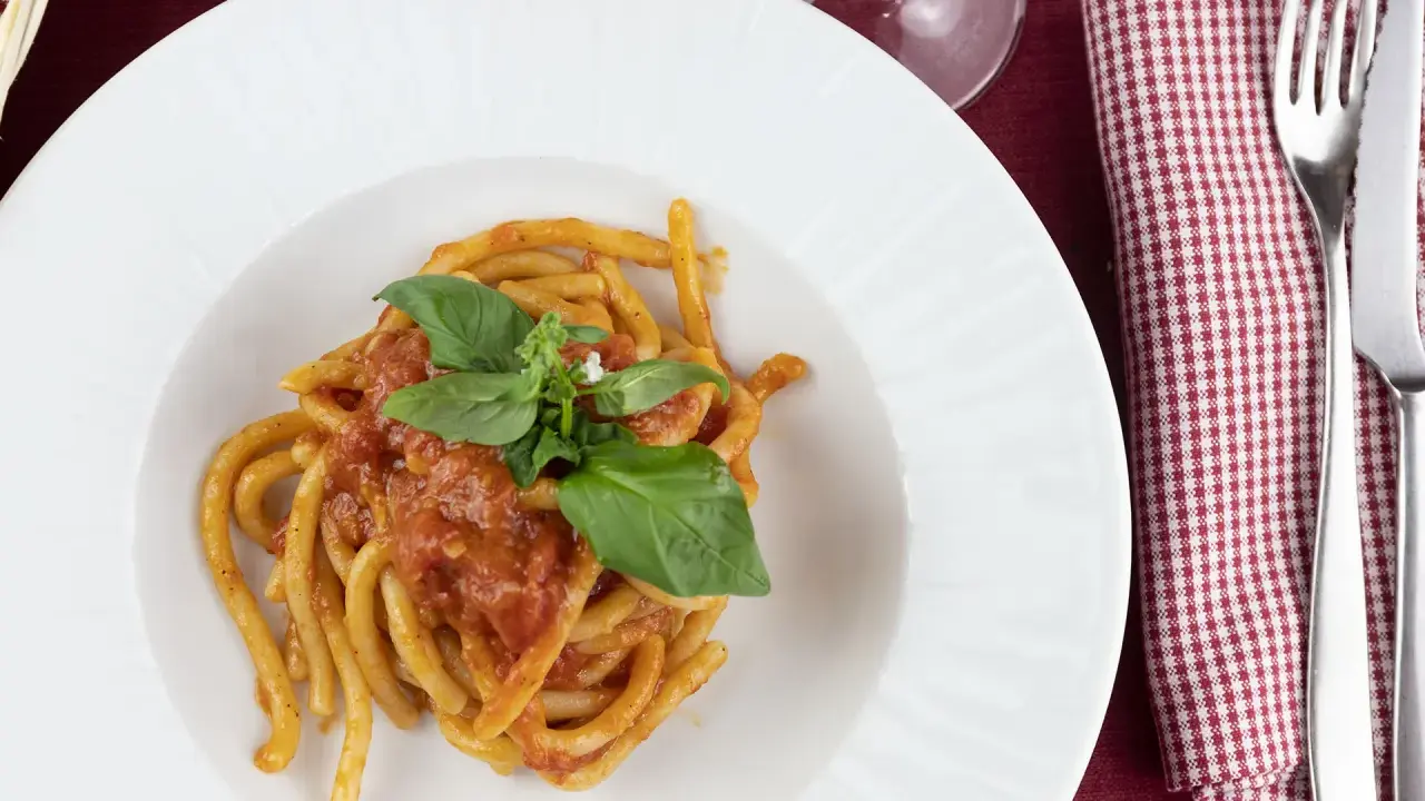 Pici al sugo, un classico della ricetta aglione Val di Chiana, serviti su un piatto bianco con basilico fresco.
