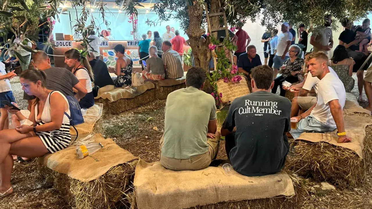 Gente seduta su balle di fieno sotto alberi, un evento estivo in Sicilia.