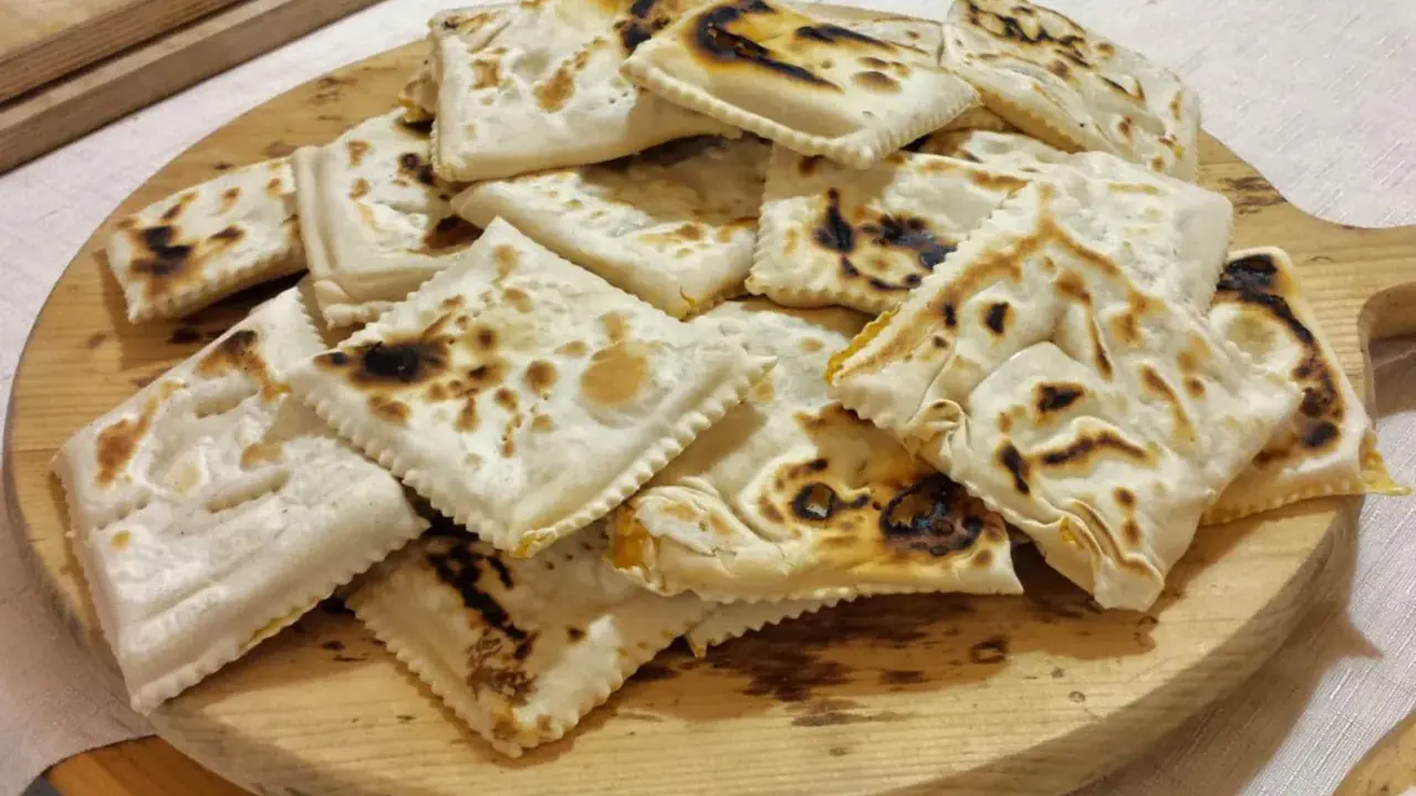 Piatto tipico cesenate: piadina fritta, dorata e leggermente bruciacchiata, servita su un tagliere di legno.