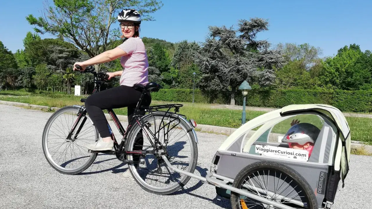 Donna in bici con rimorchio per bambini, pronta per le vacanze in bici con bambini.