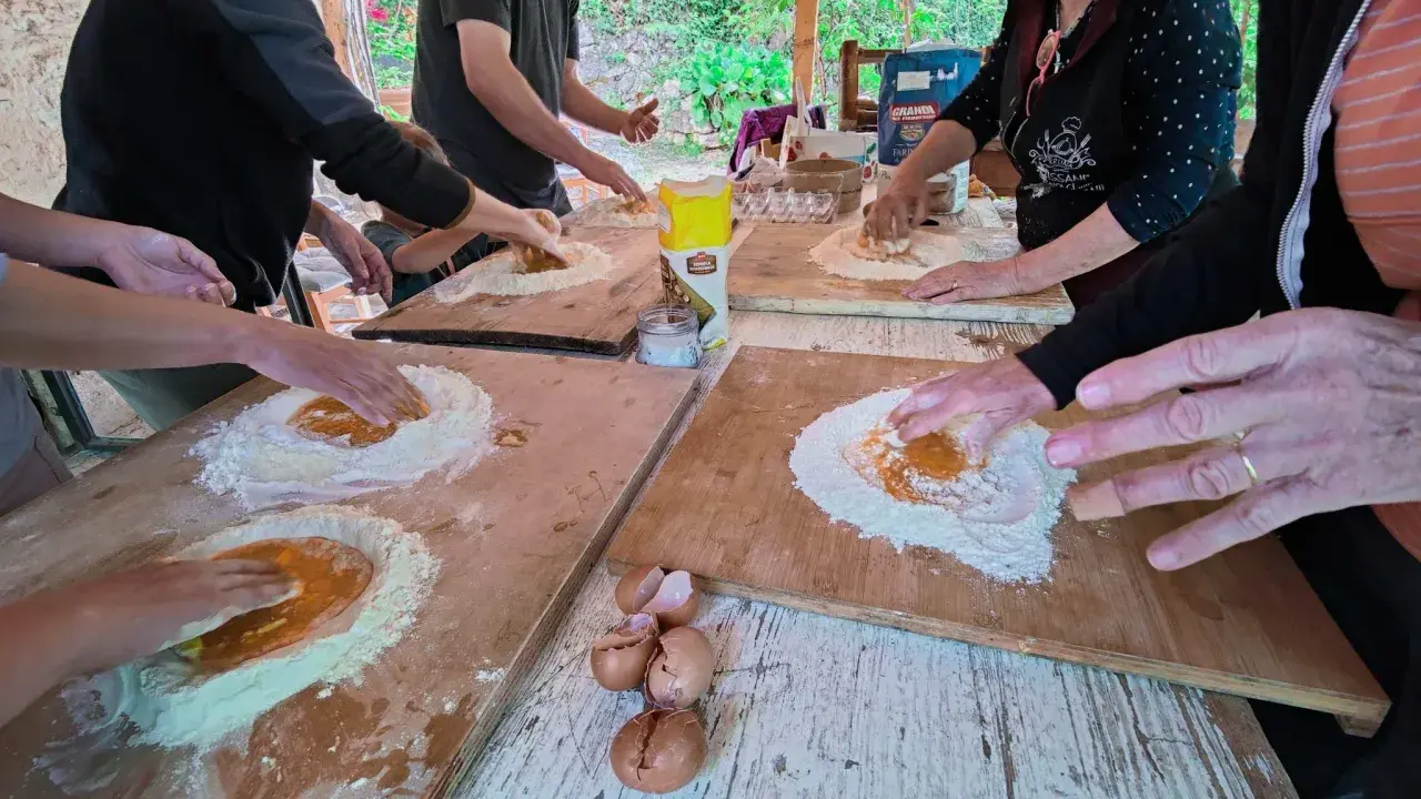 Bambini e adulti impastano farina e uova in una fattoria in Abruzzo, un'esperienza culinaria all'aperto.