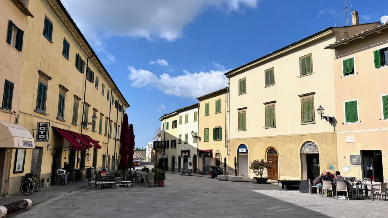 Piazza soleggiata a Pomarance, con edifici storici, tavolini all'aperto e scorci suggestivi da scoprire.