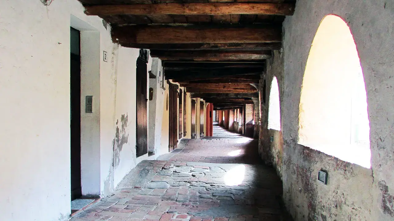 Portico con soffitto in legno e archi luminosi, pavimentazione in mattoni antichi. Un viaggio nella storia lungo la via degli asini a Brisighella.