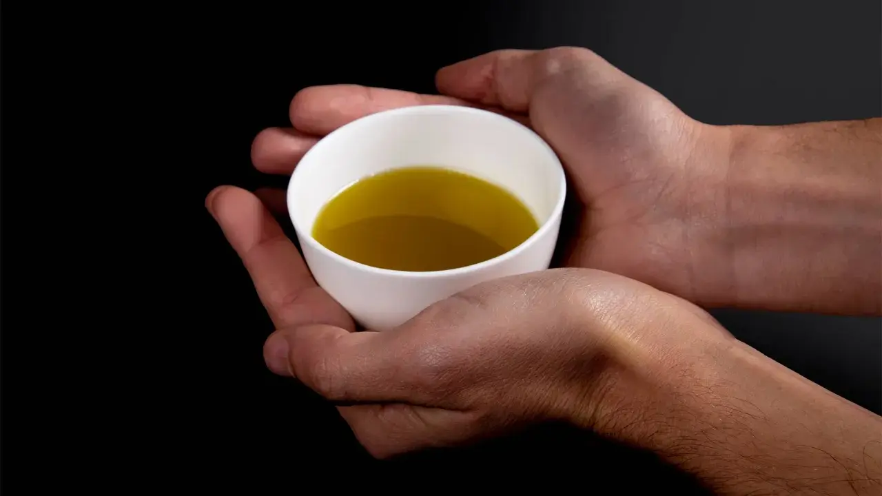Mani che sorreggono una tazzina bianca con olio evo. Il suo significato è prezioso, un nettare dorato.