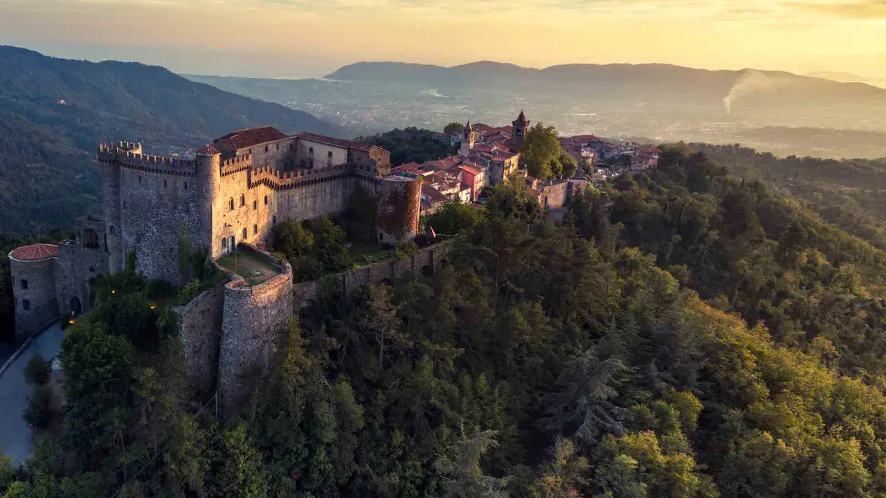 Antico castello medievale su una collina boscosa, uno dei tanti castelli da visitare in Toscana, con un villaggio arroccato e vista sulla valle al tramonto.