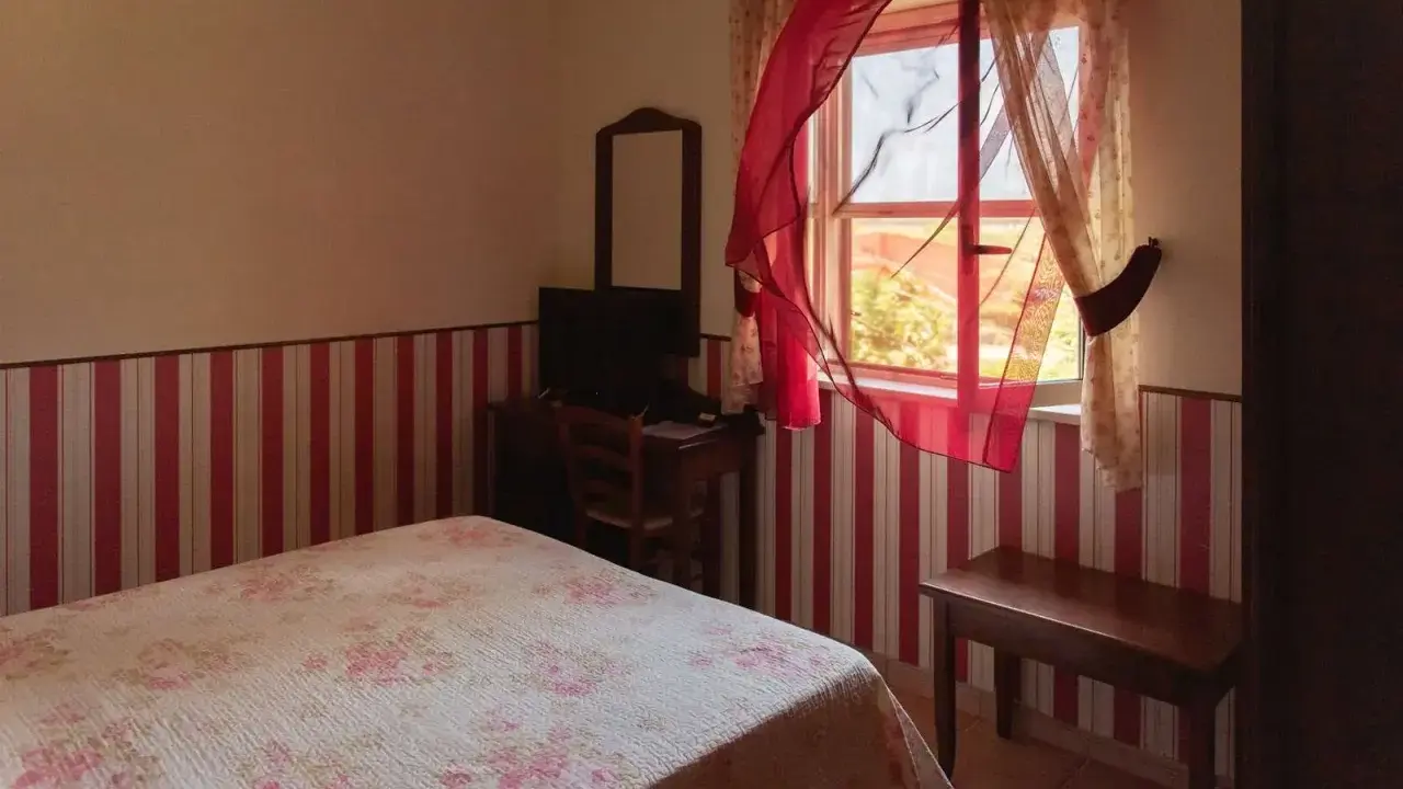 Camera accogliente in un agriturismo a Lamezia Terme, con letto fiorato e tende rosse che danzano al vento.
