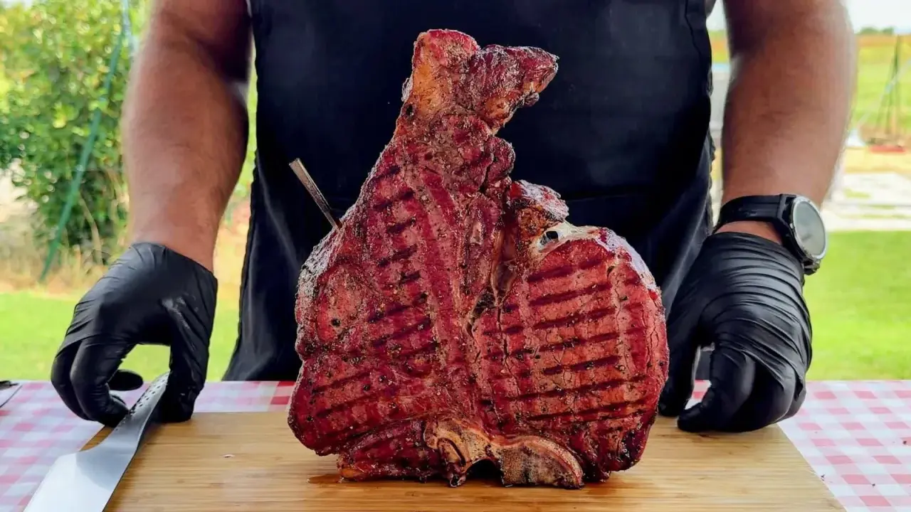 Un cuoco con guanti neri mostra una succulenta bistecca alla fiorentina appena grigliata, pronta per essere servita. Un esempio perfetto di come cucinare la bistecca alla fiorentina.