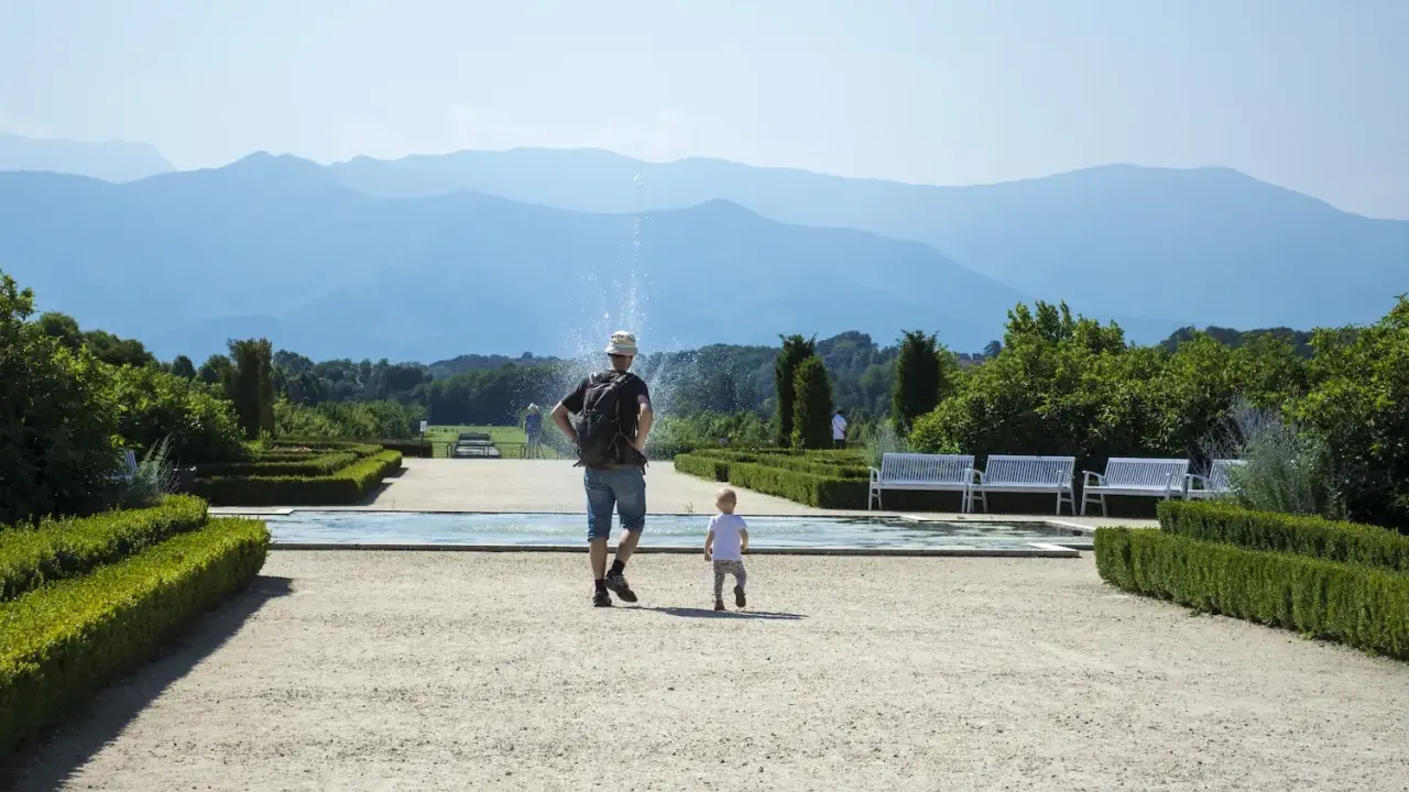 Un uomo e un bambino passeggiano in un giardino curato, con fontane e montagne sullo sfondo. Una giornata perfetta in Piemonte con bambini.